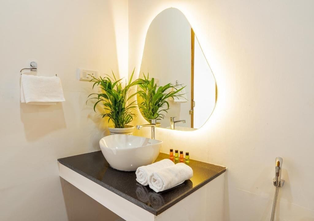 Un baño con un lavamanos blanco, un espejo, una toalla, una planta en maceta y una ducha.