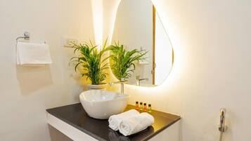 Un baño con un lavamanos blanco, un espejo, una toalla, una planta en maceta y una ducha.