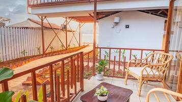 A balcony with a wooden railing, a table with a potted plant, and wicker furniture.