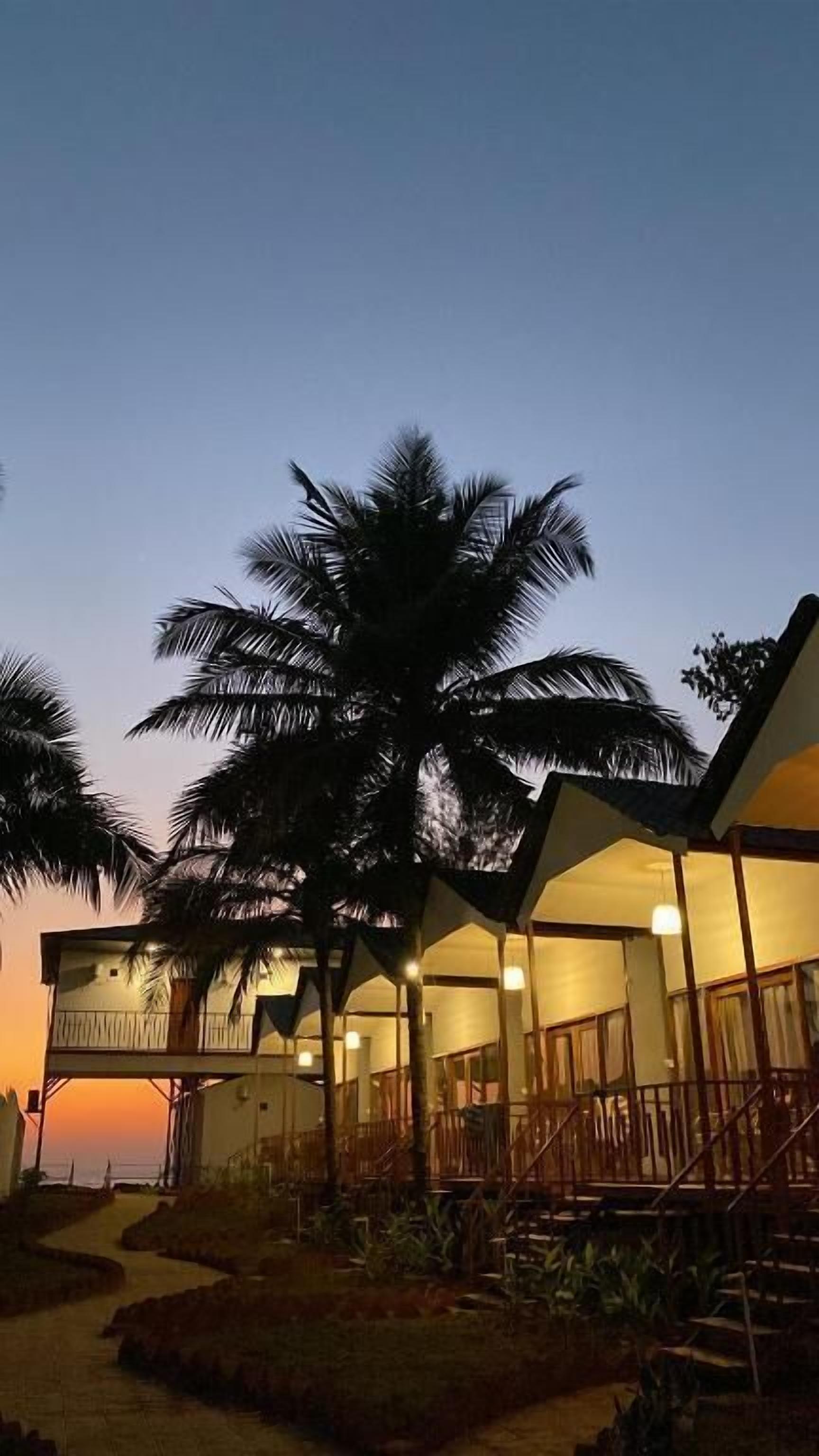 Un resort con múltiples bungalows sobre el agua, palmeras y cielo despejado.