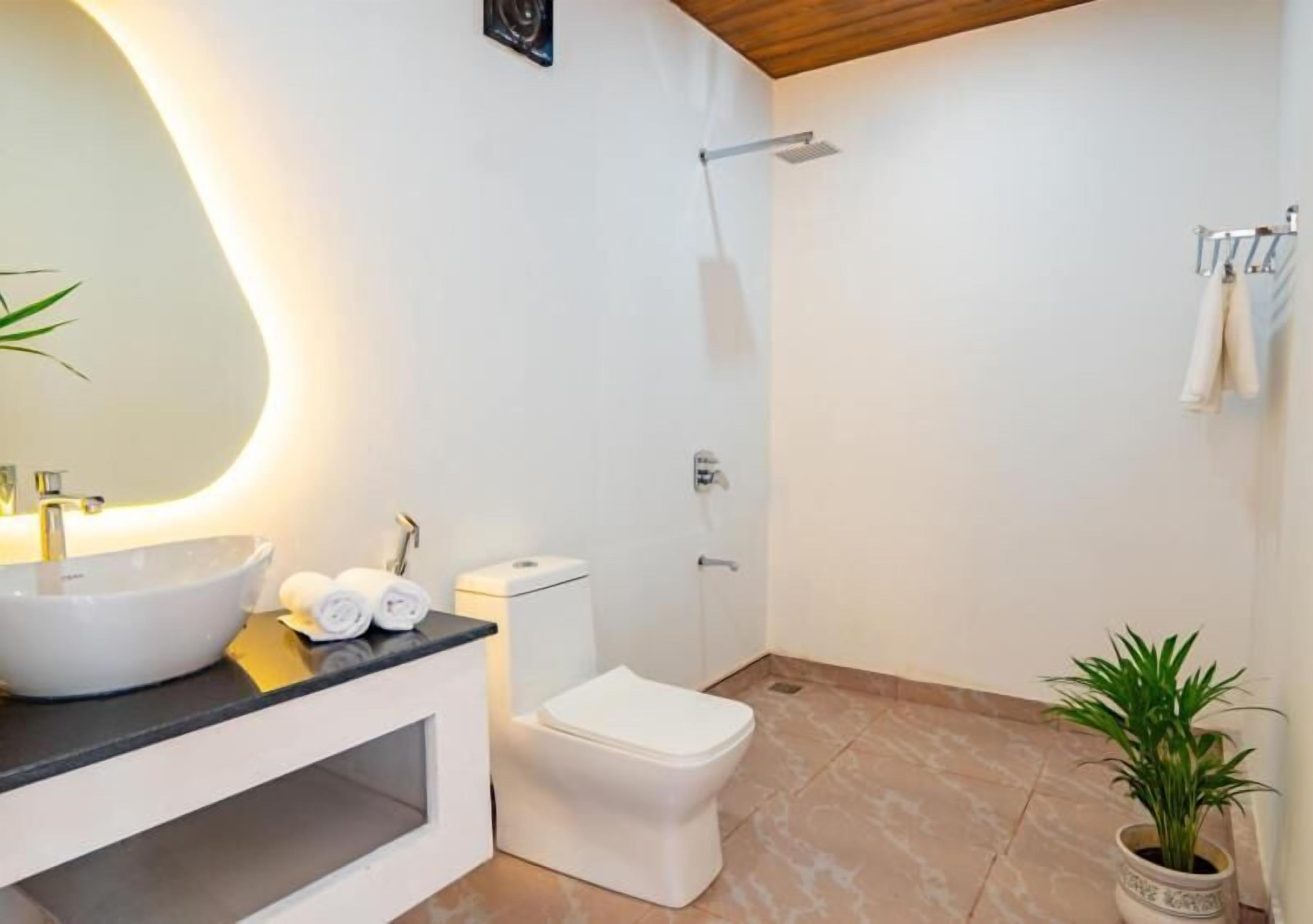 Un baño moderno con un espejo grande, un lavabo blanco, un inodoro y una ducha.