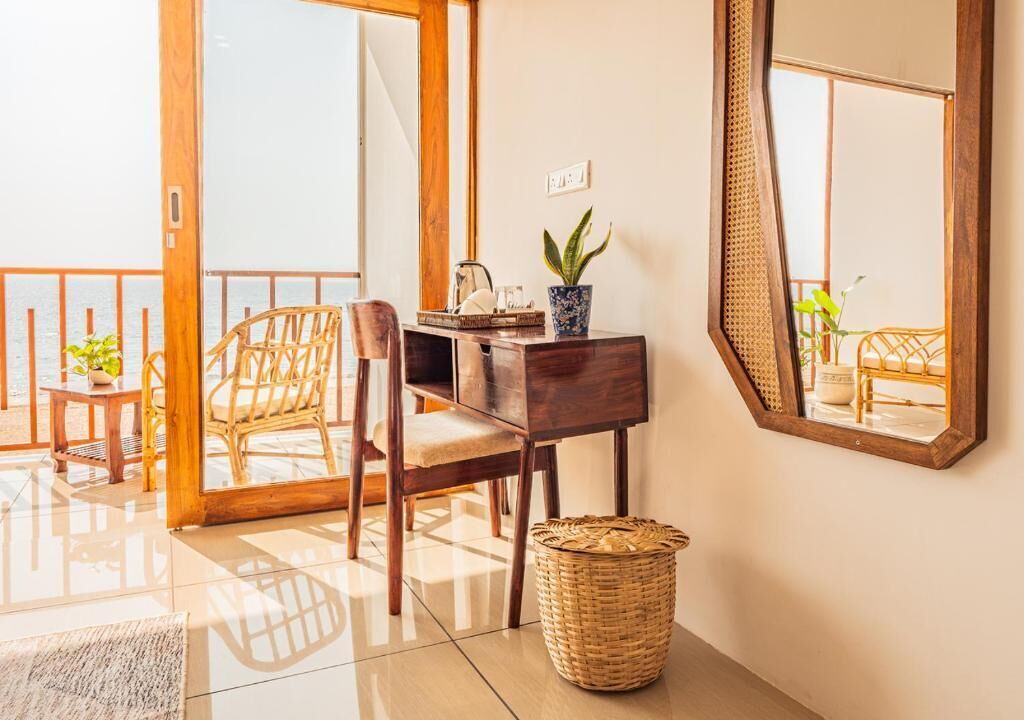A room with a wooden desk, wicker chair, and a large mirror on the wall.