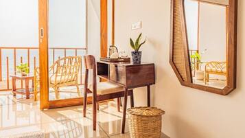 A room with a wooden desk, wicker chair, and a large mirror on the wall.