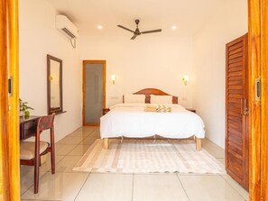 Un dormitorio con cama, mesitas de noche, ventilador de techo y puerta de madera.