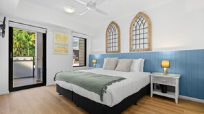 Ein Schlafzimmer mit einem Bett, Nachttischen, einem Deckenventilator und Blick durch eine Schiebetür.