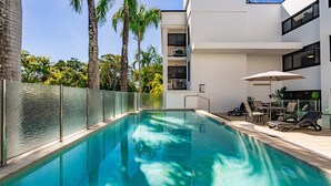 Ein Swimmingpool mit Glaszaun, Liegestühlen und einem Tisch mit Sonnenschirmen.