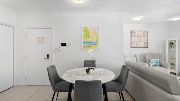 Un salón moderno con una mesa redonda de mármol, sillas tapizadas en gris, un sofá gris y una obra de arte colgada en la pared.