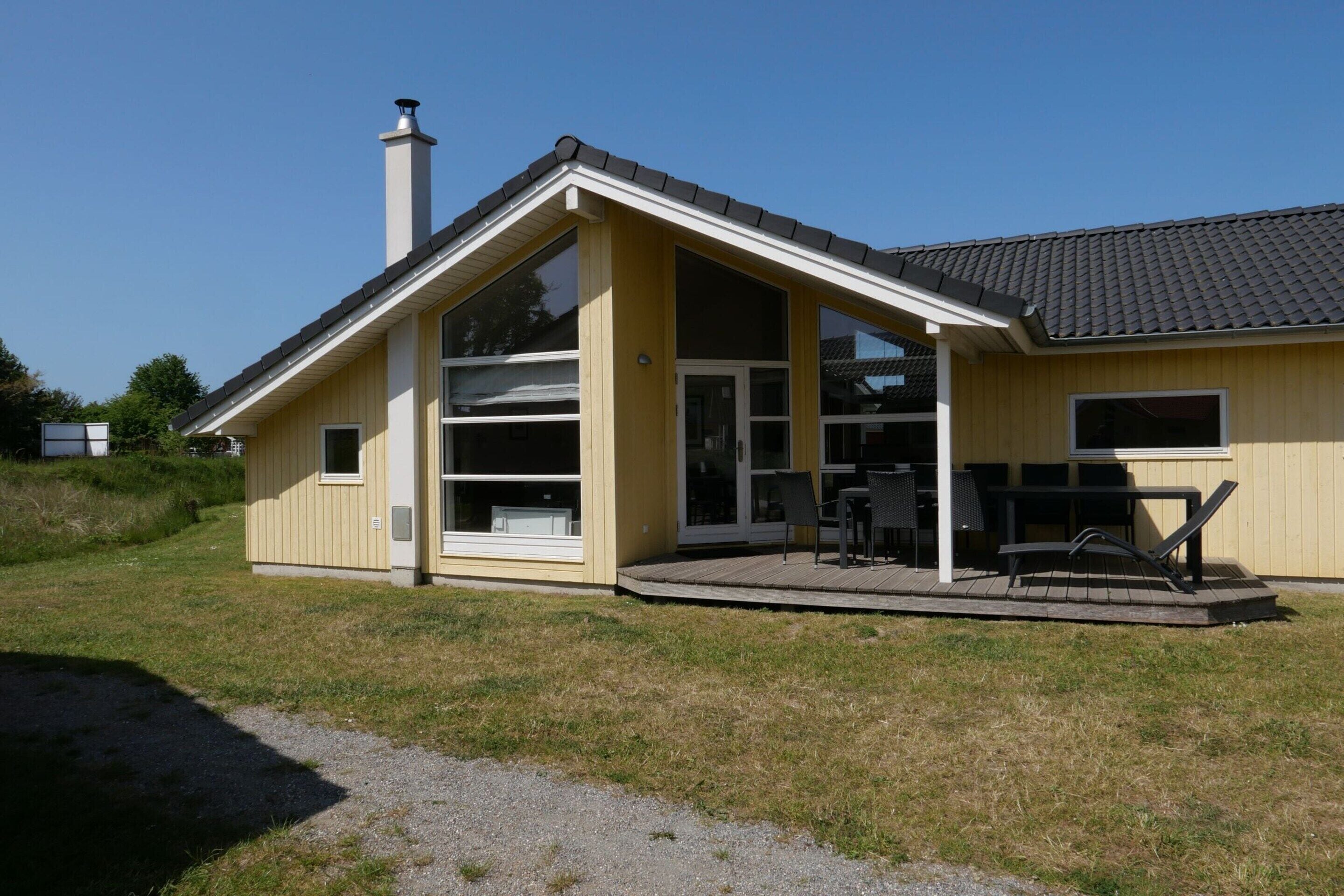 Yhden kerroksen rakennus, jossa on suuri lasiovella varustettu sisäänkäynti, katettu terassi ulkokalusteineen ja savupiippu.