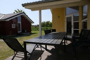 A covered outdoor dining area with a table and chairs, a red building, and a yellow building with a sliding glass door. - Grobenbrode Pine-edge Spa Retreat (Grossenbrode)