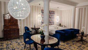 Camera d'albergo con un'ampia lampadario, un letto, un divano blu, un comò in legno e un tappeto decorato.