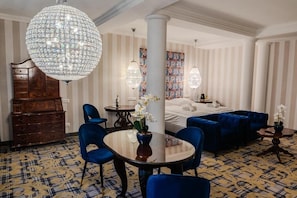 Habitación de hotel con un gran candelabro, una cama, un sofá azul, un aparador de madera y una alfombra estampada.