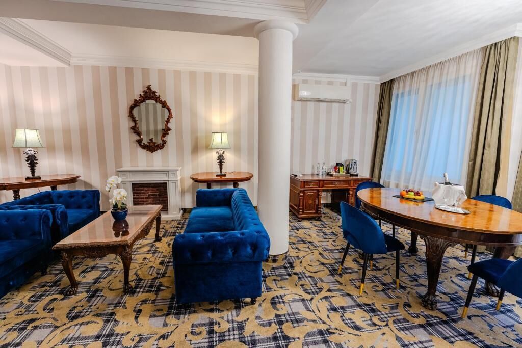Une chambre d’hôtel avec une cheminée, une table à manger avec des chaises, un canapé et un grand miroir au mur.