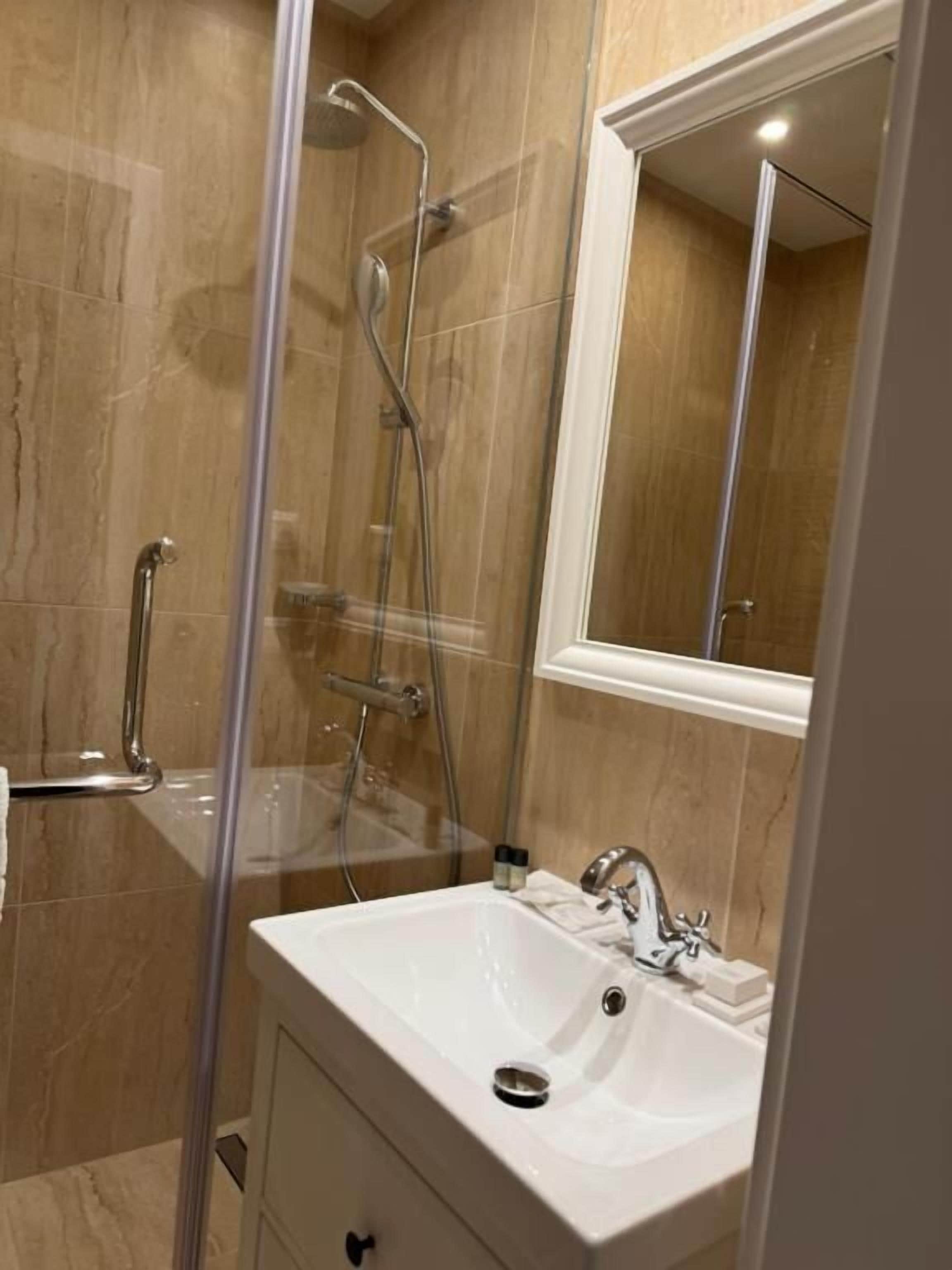 Ein Badezimmer mit einer Duschkabine, einem weißen Waschbecken und einem Spiegel darüber.