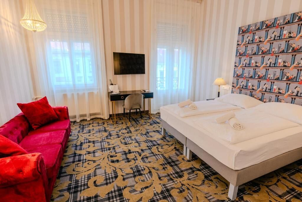 Una camera d'albergo con un letto, una scrivania, una sedia, un divano rosso e un tappeto decorato.