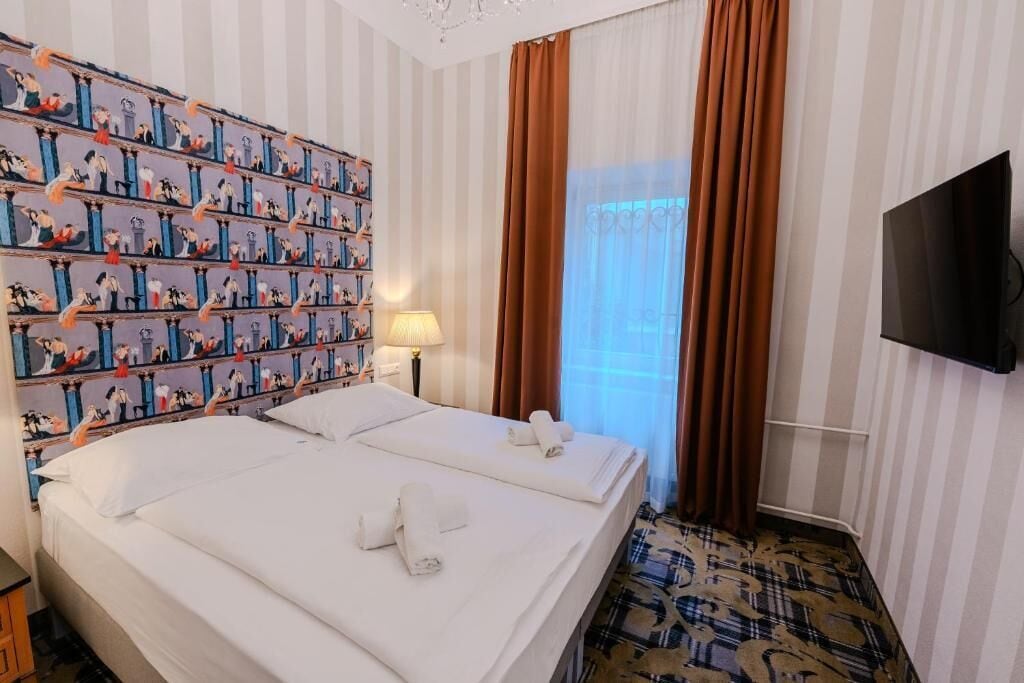 A hotel room with two beds, a television, a patterned carpet, and a striped wall with a curtain.