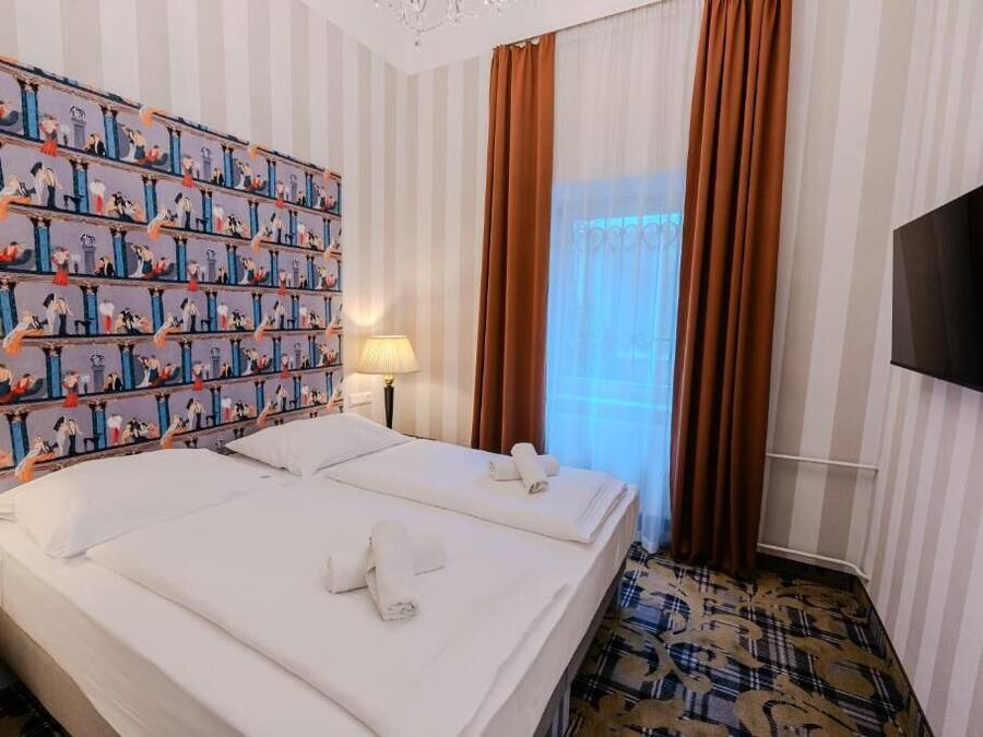 A hotel room with two beds, a television, a patterned carpet, and a striped wall with a curtain.