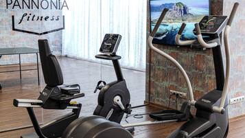 Un gimnasio con máquinas de cardio, un televisor mostrando una vista panorámica y un cartel con el año de fundación.