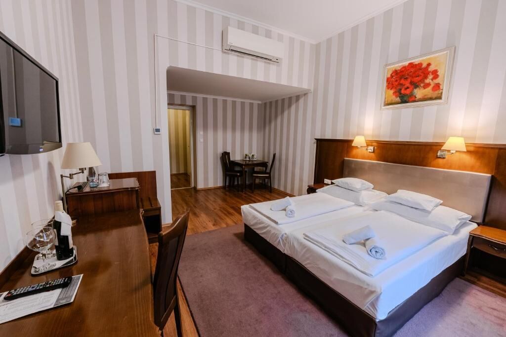 Ein Hotelzimmer mit Bett, Nachttischlampen, einem Schreibtisch mit Lampe, einem Fernseher und einem Bild an der Wand.