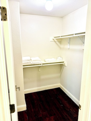 Ein Zimmer mit Holzboden, weißen Wänden und einer Tür. Weiße Regale mit gefalteten Handtüchern sind vorhanden.