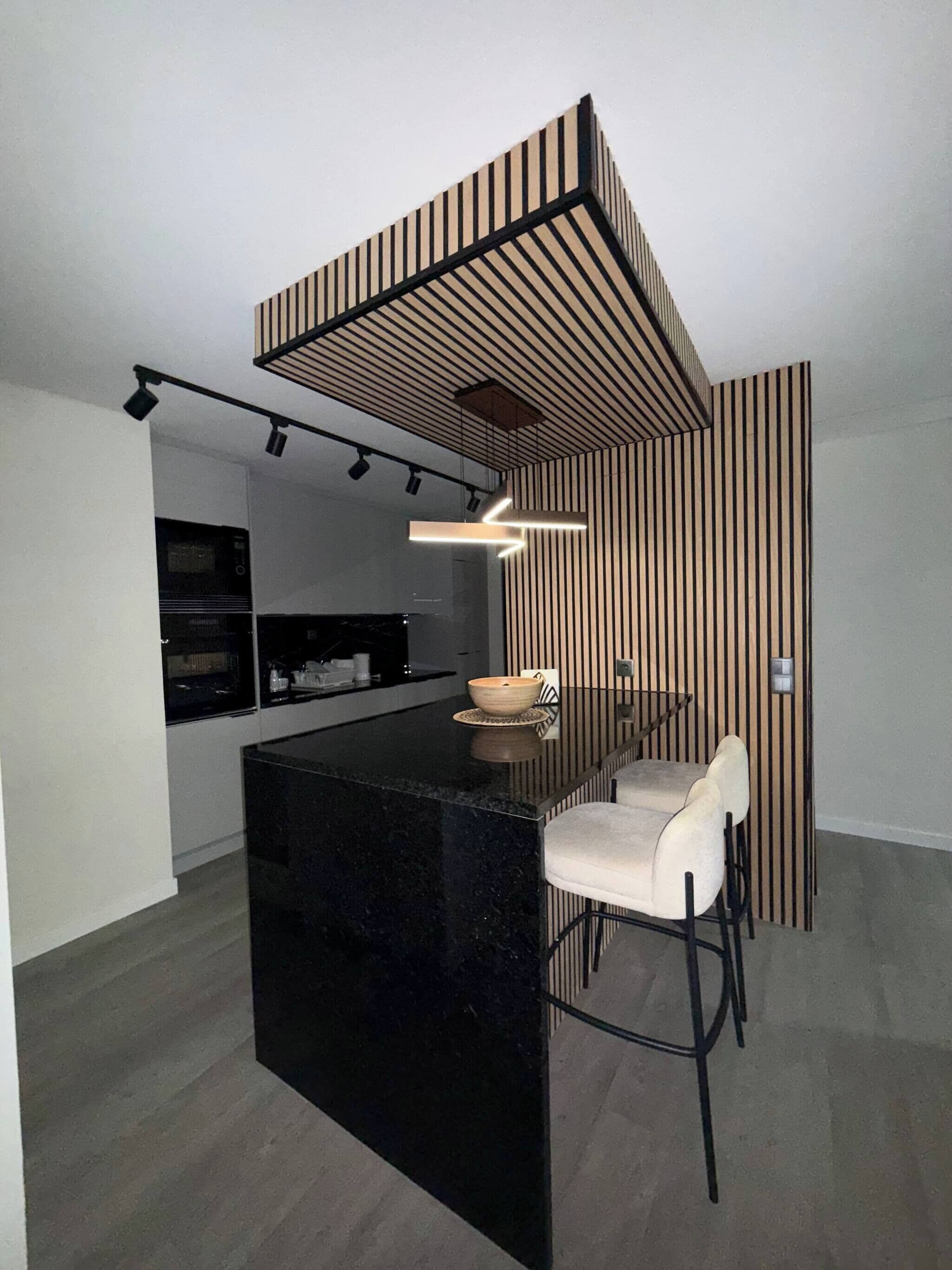 A modern kitchen with a black countertop, a built-in oven, and a dining area with a white chair and a bowl on the island.