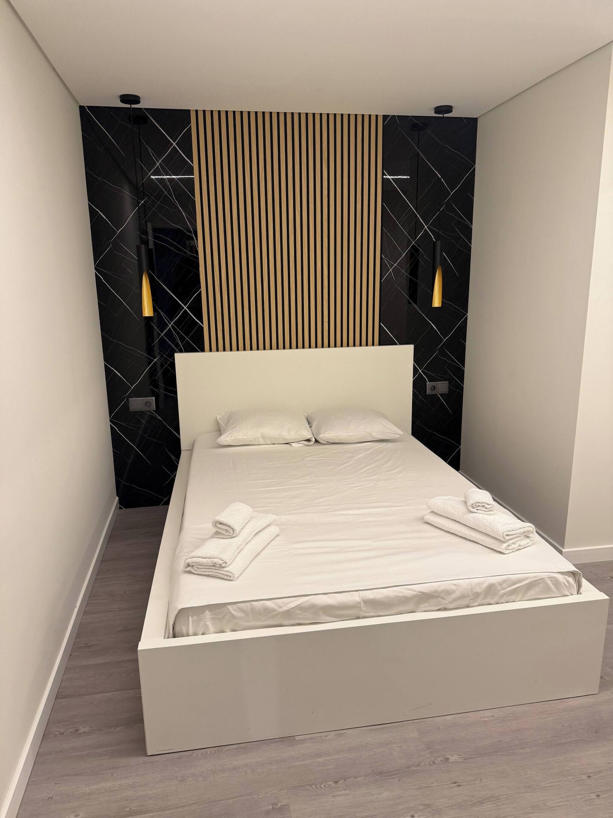 A modern bedroom with a large bed, a wooden slat wall, and two wall-mounted lights.