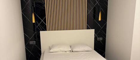 Une chambre moderne avec un grand lit, un mur recouvert de lambris en bois et deux lampes fixées au mur.