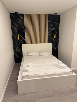 A modern bedroom with a large bed, a wooden slat wall, and two wall-mounted lights. - Luxury 3BR Apartment 2 Baths Near Lisbon & Sintra (Sintra)