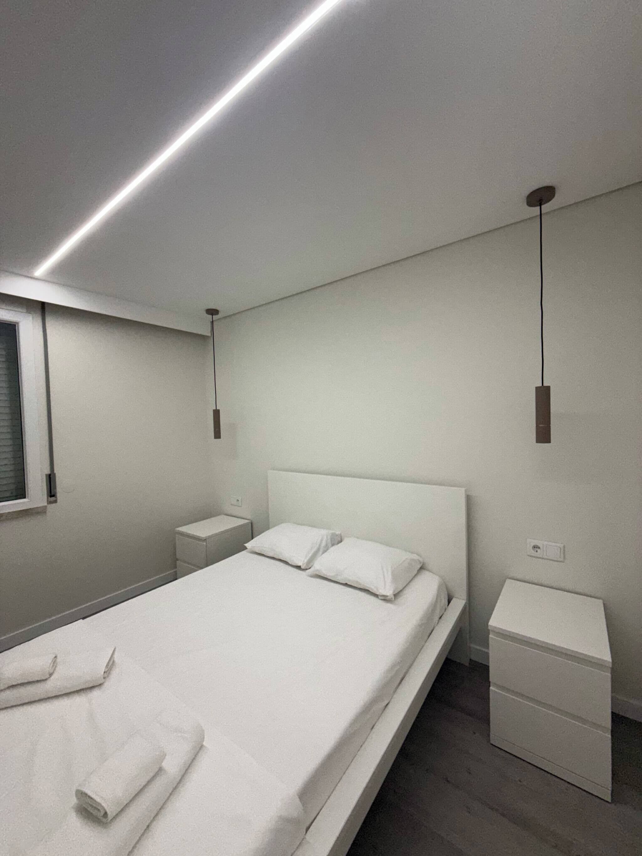 Un dormitorio moderno con una cama individual, mesitas de noche y una lámpara colgante.