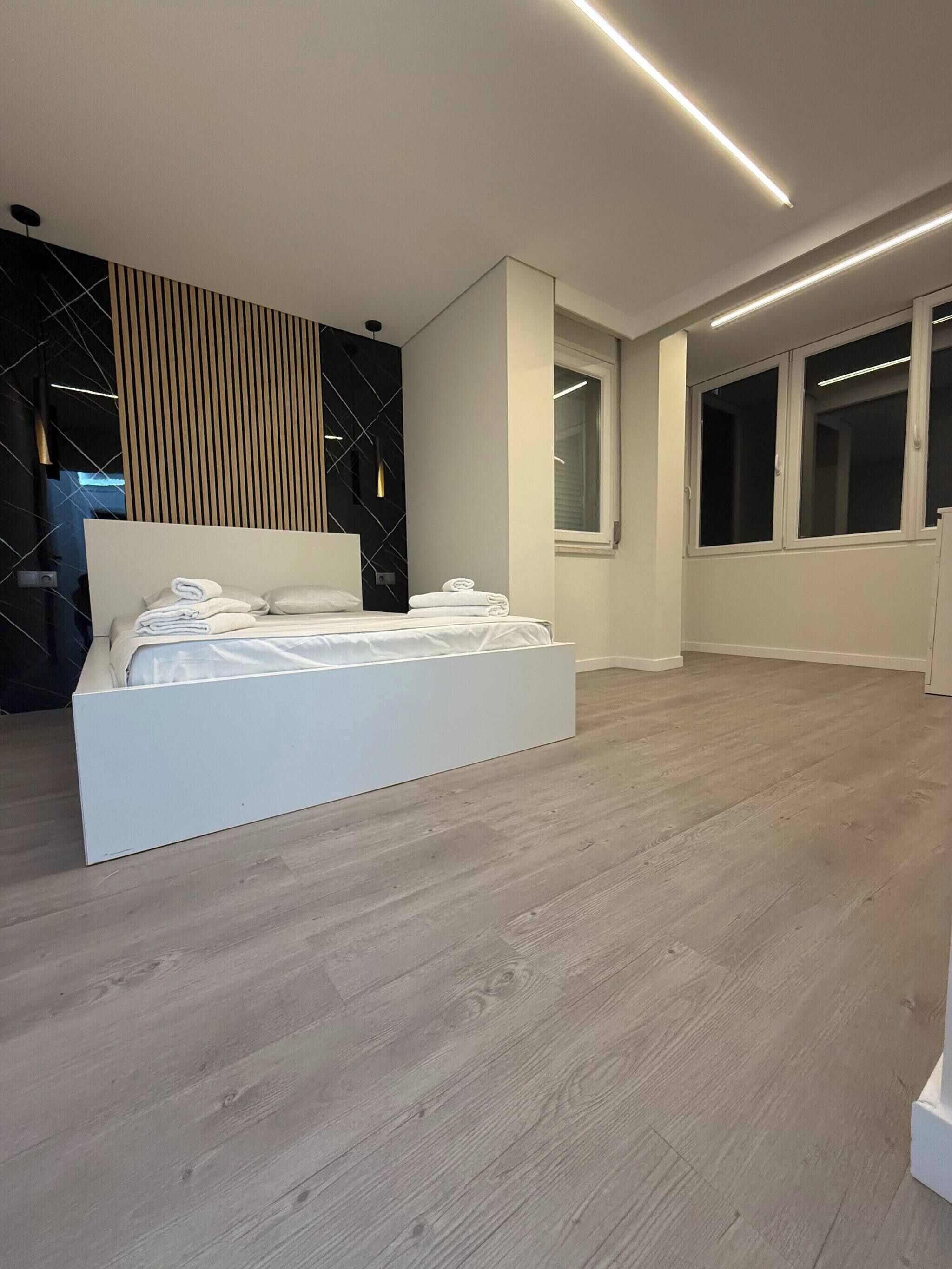 Une chambre moderne avec un grand lit, un mur d’accent en bois et une fenêtre avec des stores.