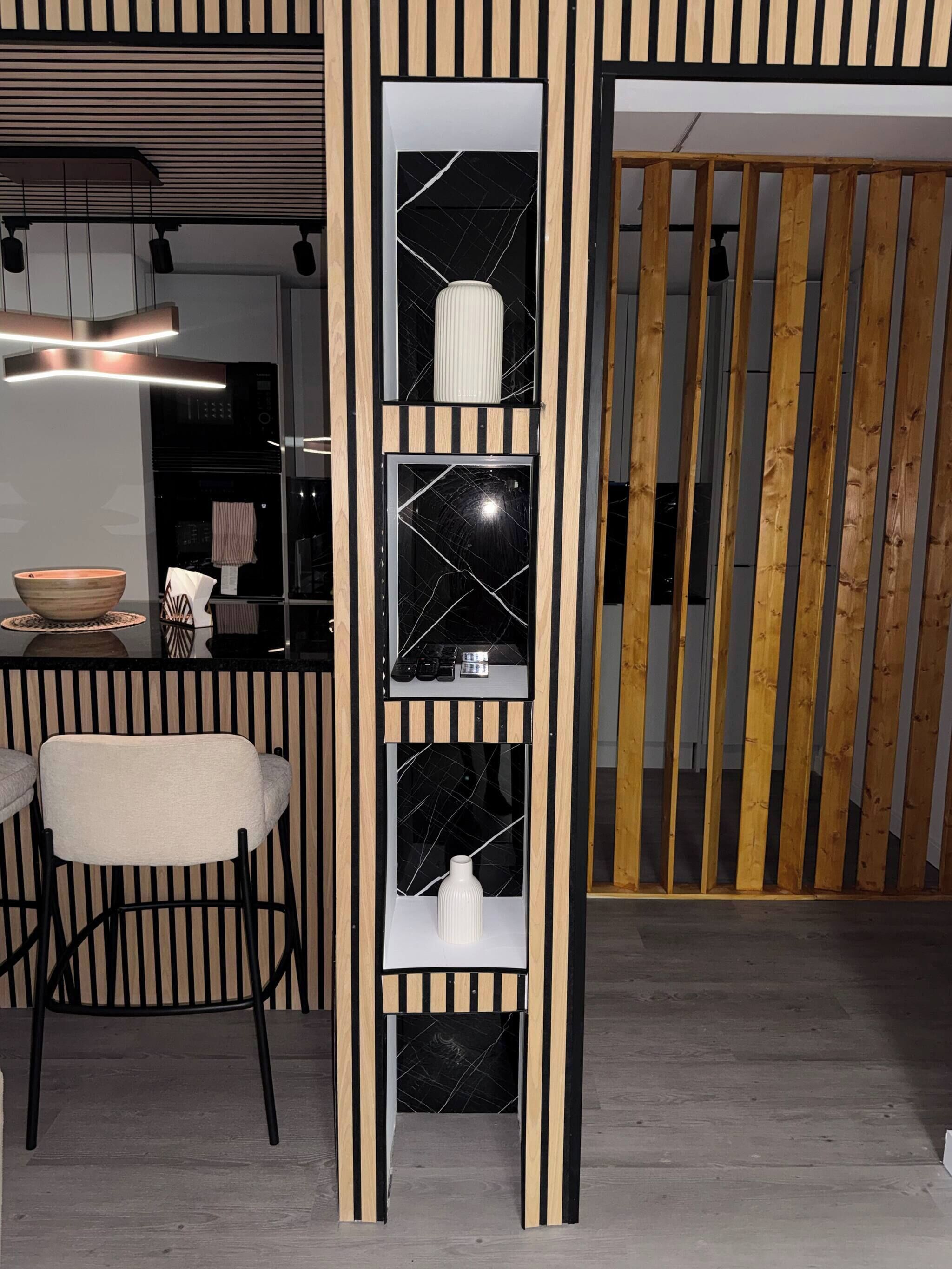 A modern interior with a black and white striped partition, a white ribbed vase on a shelf, and a bar area with a bowl and bar stools.