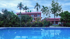 Una piscina con el reflejo de palmeras y un edificio de techo rojo al fondo.