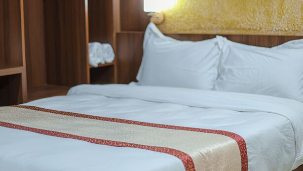 Habitación de hotel con cama, cabecero de madera y estante con una toalla.