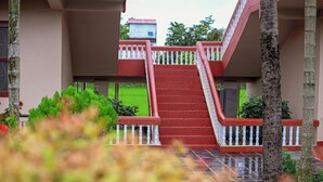 Una escalera conduce a un edificio con barandilla roja y blanca, rodeado de vegetación.