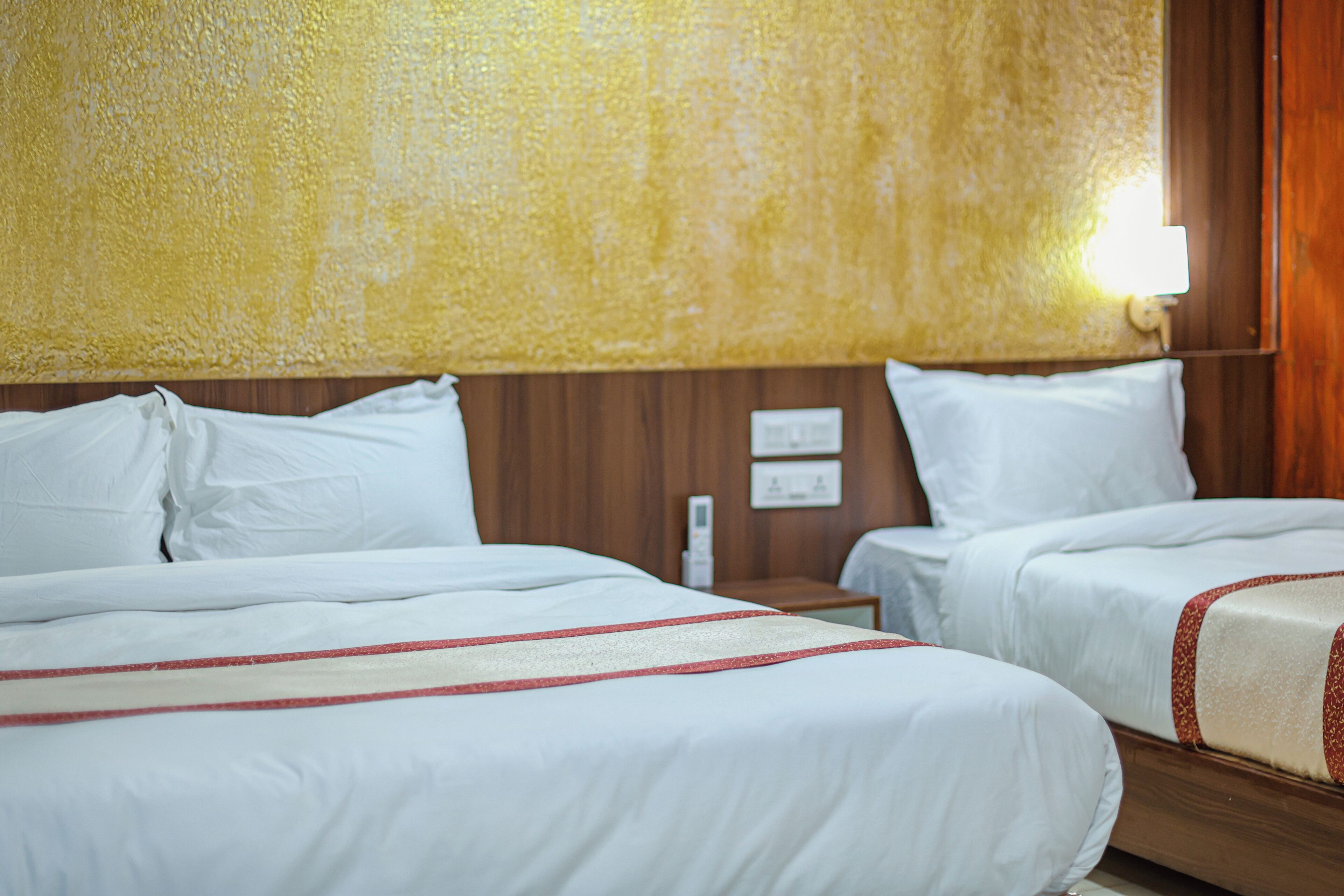 Habitación de hotel con dos camas, cabecero de madera, ropa de cama blanca y una mesita de noche con lámpara.