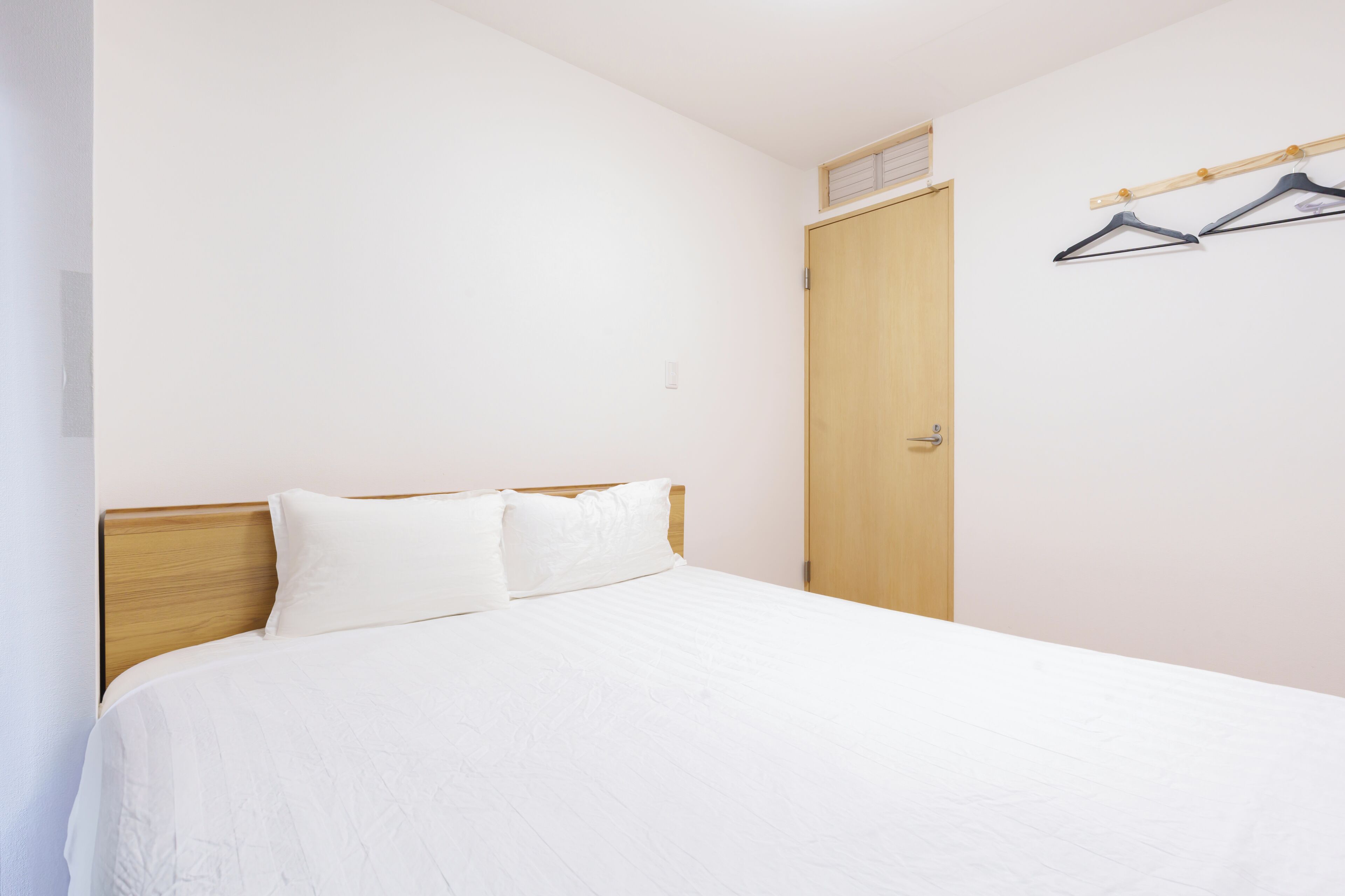 A single bed with a wooden headboard, a wooden door, and a clothes hanger on the wall.