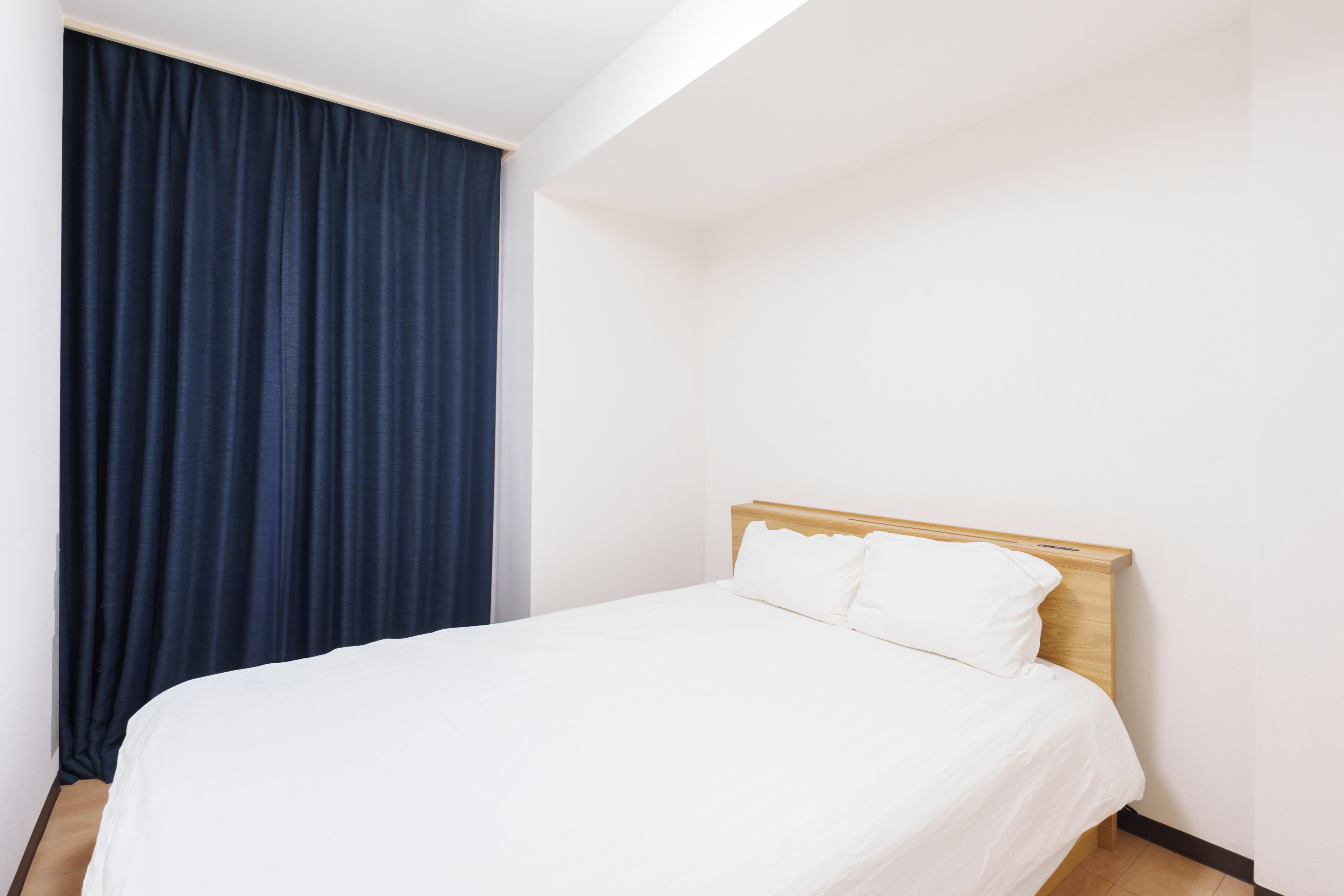 Een hotelkamer met een eenpersoonsbed, een houten hoofdbord en een donkerblauwe gordijn.