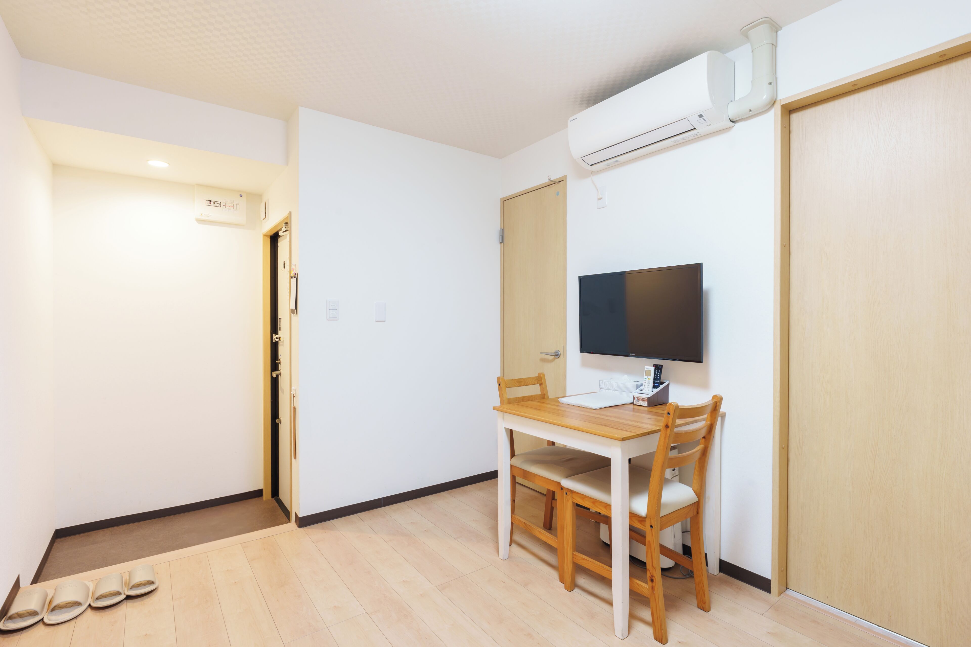 A room with a wooden desk, a chair, a television, and a wardrobe.