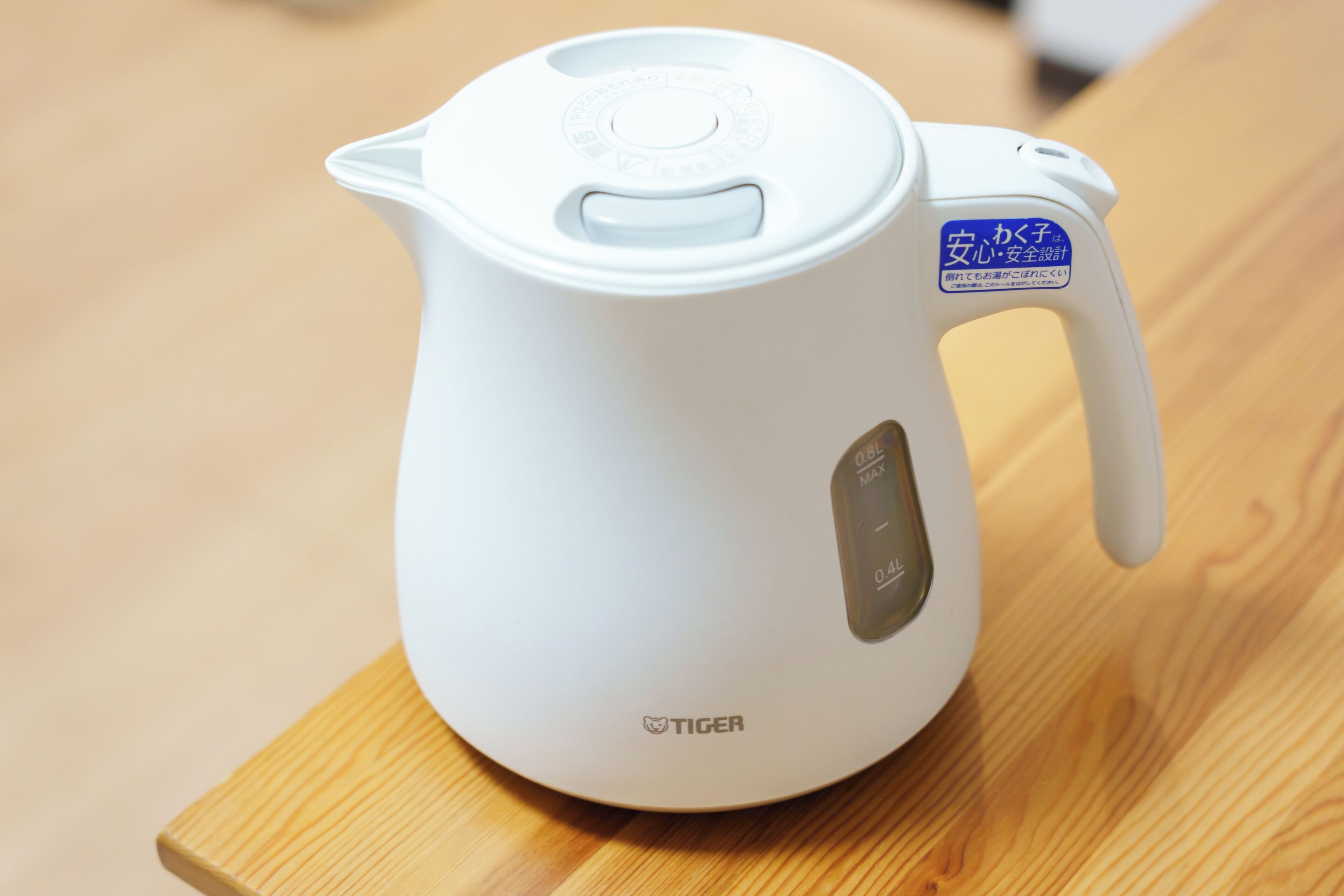 A white electric kettle with a handle and a blue safety instruction label on a wooden surface.