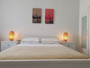 Een slaapkamer met een bed, twee bedlampjes, een nachtkastje en twee aan de muur hangende schilderijen.