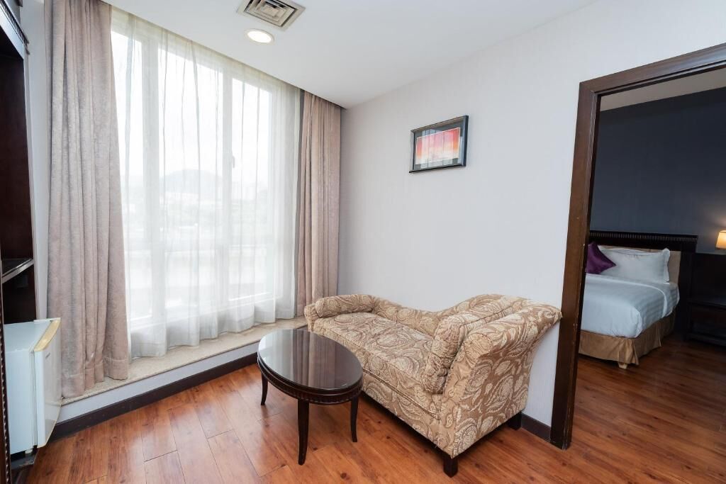 A hotel room with a sofa, a small table, a bed, and a window with curtains.