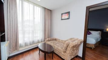 A hotel room with a sofa, a small table, a bed, and a window with curtains.