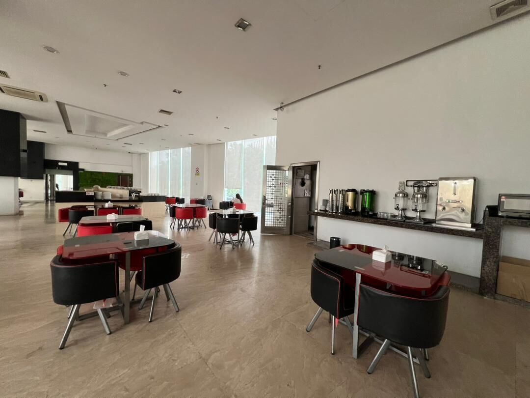 A spacious dining area with multiple tables and chairs, a kitchen area with appliances, and a large window providing natural light.
