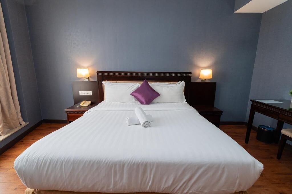 A hotel room with a large bed, two bedside lamps, a wooden nightstand, and a small table with a lamp.