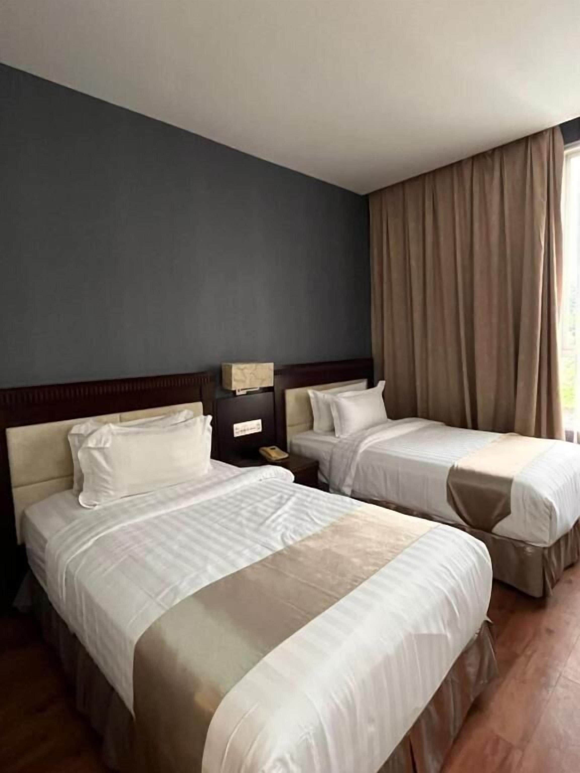 A hotel room with two beds, a nightstand, and a window with curtains.