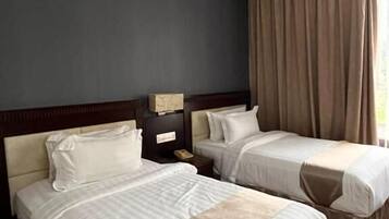 A hotel room with two beds, a nightstand, and a window with curtains.