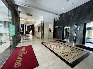 Un vestíbulo de hotel con alfombra roja, pisos de mármol y una recepción.