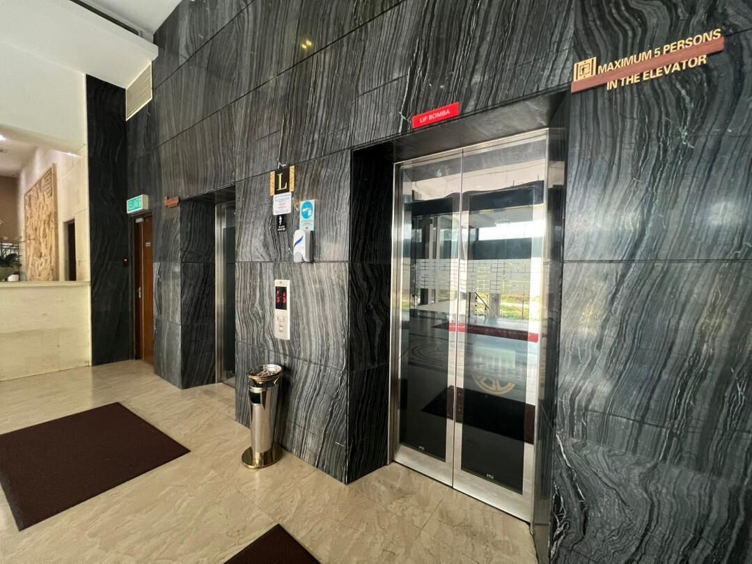 A modern elevator with a marble wall, a sign indicating a maximum of 5 persons, and a trash bin.