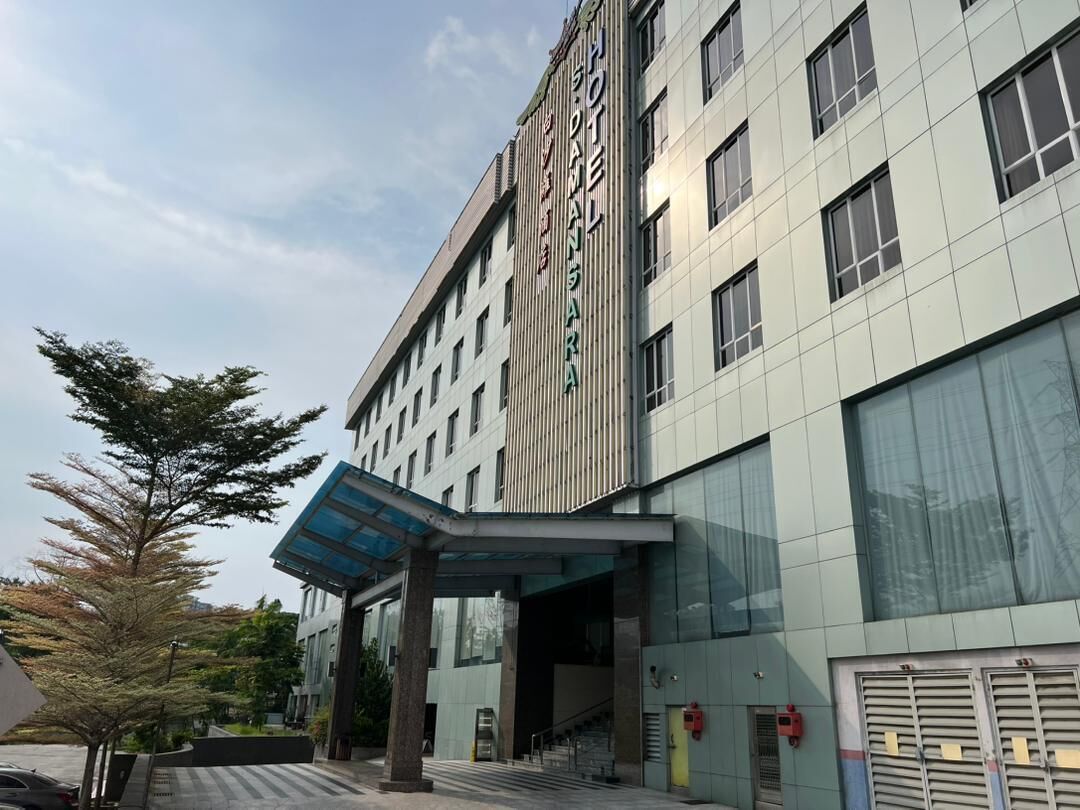 A modern hotel entrance with a covered entrance, large windows, and a visible staircase leading to the lobby.