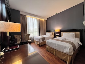 Una habitación de hotel con dos camas, un escritorio, una silla, una lámpara y una ventana con cortinas.