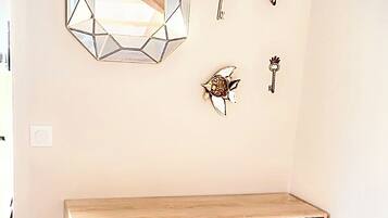 Un bureau en bois doté de tiroirs et d’une étagère, un miroir aux motifs géométriques et des clés décoratives accrochées au mur.
